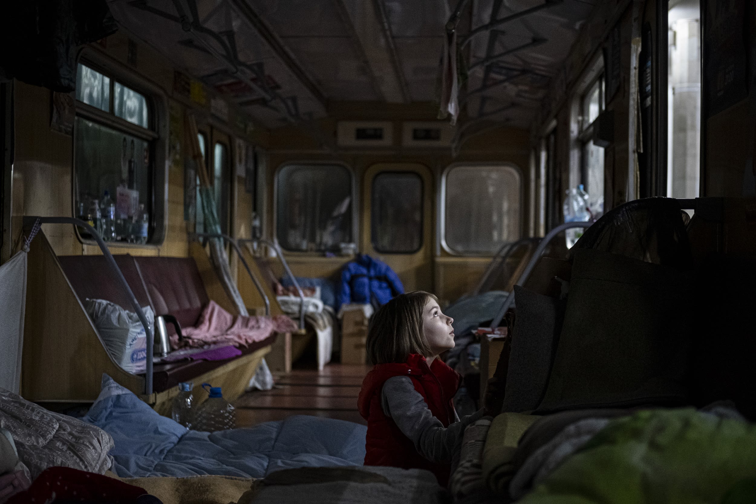 A girl sitting on the floor of a subway train car looks up toward a window.