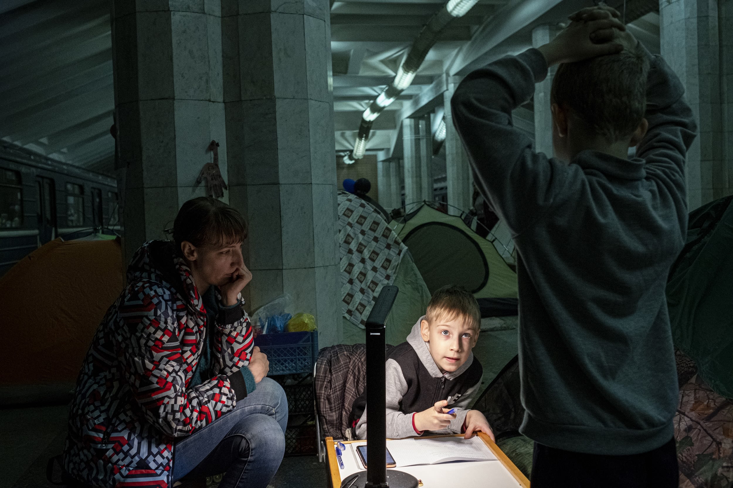 A child does his homework by the light of a lamp in a subway station.